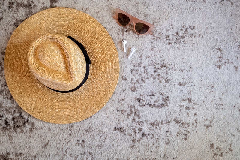 flat layout of sun hat, sunglasses, and airpods on a beach